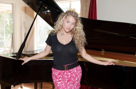 Adorable blonde Emily R shows her cleavage in front of the piano